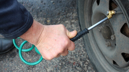 In a man's hand there is a hose from a compressor pumping up a car wheel. Close-up.