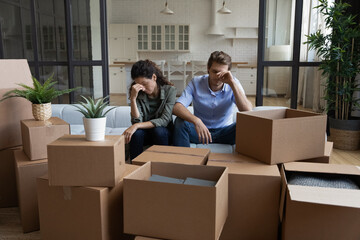 Tired unhappy young Caucasian couple sit on sofa in new living room feel unmotivated unpacking....