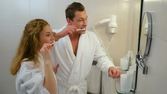 Man and woman bathrobes cleaning brushing teeth together in bathroom before mirror. Family in hotel on vacations. Luxury resting concept. Young couple in love in honeymoon. Morning routine.