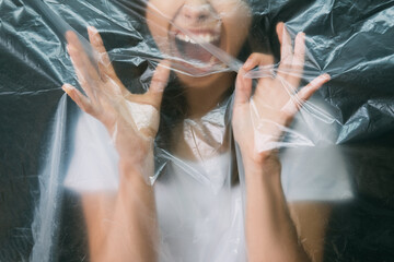 Mental disorder. Defocused silhouette. Nervous breakdown. Cropped portrait of frustrated woman yelling trapped behind creased polyethylene film isolated on black background out of focus.