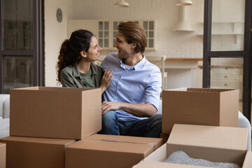 Happy millennial man and woman sit relax on sofa in living room enjoy moving day to new apartment together. Smiling young Caucasian couple renters celebrate relocation to own home. Rental concept.