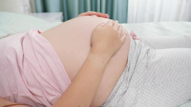 CLoseup of pregnant woman before childbirth lying on hospital bed and touching her big belly. Concept of pregnancy, preparing and expecting child.