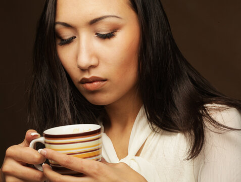 Young asian woman holding a coffee cup over brown background, close up picture