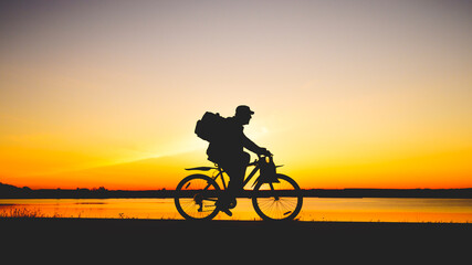 Fototapeta na wymiar Silhouette of unrecognizable senior adult man with backpack mountain bike against a sunset. Road trip concept. Empty Copy Space, side view