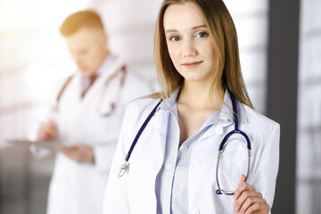 Professional beautiful woman-doctor with a stethoscope is standing straight in a sunny clinic. Young doctors at work in a hospital. Perfect medicine concept