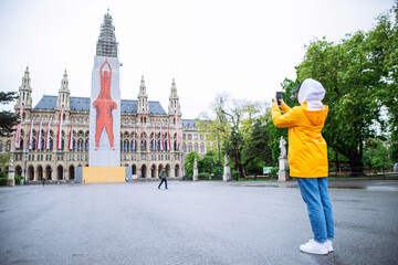 Fototapeta na wymiar Vienna, Austria - May 16, 2019: female woman tourist in yellow raincoat posing in front of city hall building