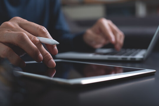 close up of man using and touching on digital tablet during working on laptop computer at home