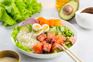 Lunch with hawaiian poke bowl with salmon fish, rice, avokado, vegetables. Sauce made of soy sauce, peanut butter, garlic and ginger. White background.