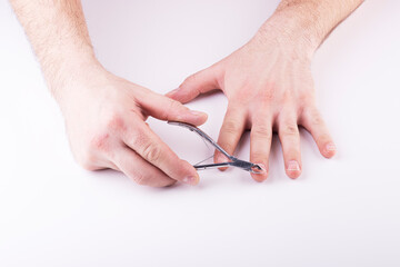 A man's hand holds a nail clipper, trimming the nails on his thumbs, on a white background