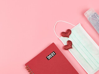  flat lay of red 2021 diary or planner, red hearts on medical face mask and alcohol sanitizer hand...