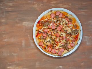 Fast homemade pizza with cheese and sausages on a white plate, cooked in a pan