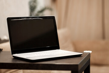 A laptop with a blank black screen in an angular position on a table against a blurred room...