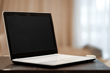 A laptop with a blank black screen in an angular position on a table against a blurred room background. The concept of workplace, office, coworking.