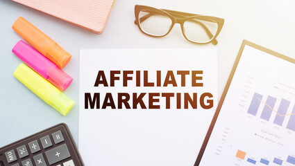 The text AFFILIATE MARKETING on office desk with calculator, markers, glasses and financial charts.