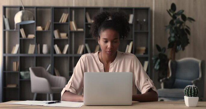 African woman working on financial paperwork seated at workplace using laptop app looks concentrated while makes task, prepare, check report having fruitful workday. Student learning process concept