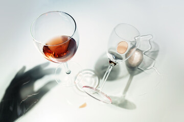 Glasses with red wine, standing and fallen in unusual perspective with reflections and a shadow of a hand on a bright background, abstract traces of a party or alcohol addiction concept