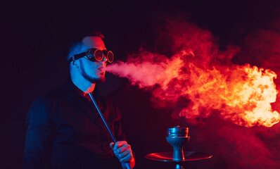 man in futuristic glasses smokes a hookah and blows a cloud of smoke in a shisha bar