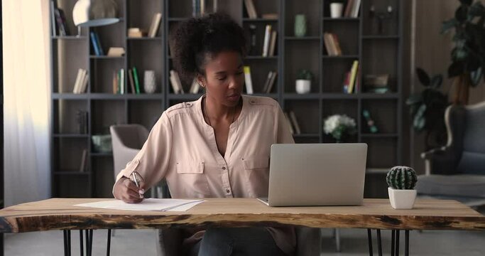 African ethnicity female manager prepare financial report making presentation writes notes or corrections do paperwork seated at modern workplace in office alone. Banking, management, finances concept