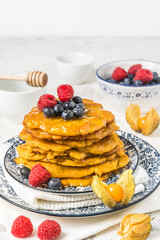 Pile of vegan pancakes with berries and syrup on white background, vertical with copy space