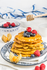 Pile of vegan pancakes with berries and syrup on a blue-white patterned plate on white background, vertical