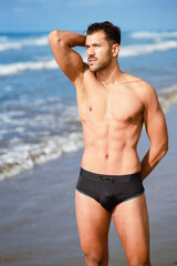 Young athletic man with fitness body standing on the beach