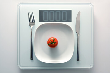 Tomato on a white plate and cutlery on a personal weight scale showing zero, healthy diet and...