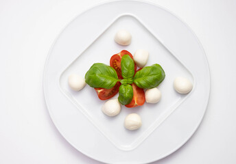 mozzarella, green basil and tomatoes on a white plate on a table