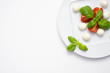 mozzarella, green basil and chopped tomatoes on a white plate on a table