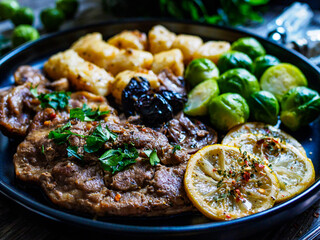 Fried pork steaks with lemon, dumplings and boiled brussels sprouts served on wooden table
