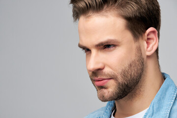 Fototapeta premium Close-up Portrait of young handsome caucasian man in jeans shirt over light background