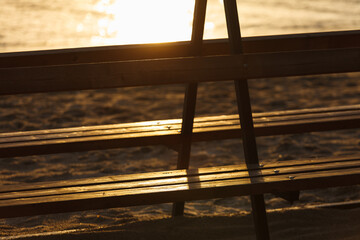 Close up view of wooden bench on the beach in the rays of the setting sun.