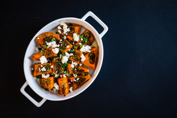 Roasted spicy pumpkin with feta cheese on black table 