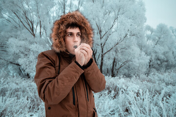 A man freezes in the cold in the forest and tries to wipe his hands with his breath. The concept of...