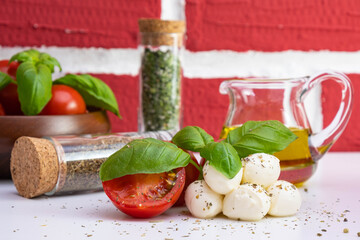 mozzarella with tomatoes and basil on a white table, near rapeseed oil in a jug and various spices