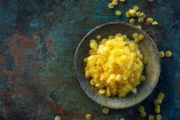 yellow beeswax pellets in ceramic plate on green grunge wooden background.
