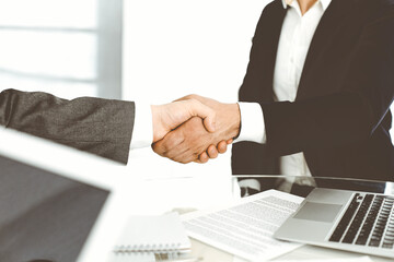 Unknown diverse business people are shaking hands finishing up meeting at the desk in office, close-up. Handshake concept