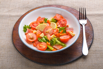 Salad with salmon and cherry tomatoes in a plate on a gray background on a wooden stand stand next to a fork.