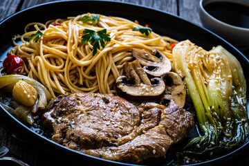Fried pork steaks with mushrooms, noodles and steamed pak choi cabbage served on wooden table
