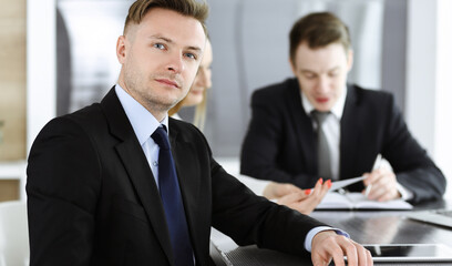 Businessman headshot at meeting in modern office. Unknown entrepreneur sitting with colleagues at the background. Teamwork and partnership concept