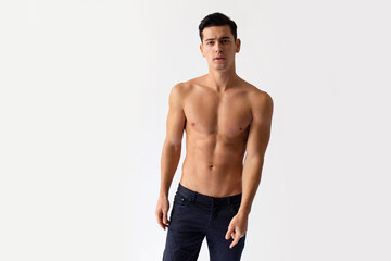 Sexy young man with nacked torso in black jeans, posing in studio, looking at camera, isolated on a white background.