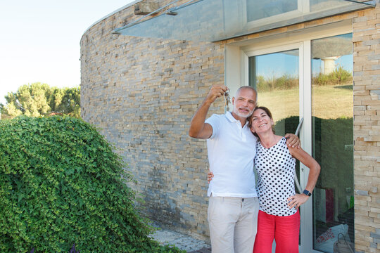 marito e moglie di mezza età mostrano le chiavi di casa mentre sullo sfondo si intravede la loro abitazione