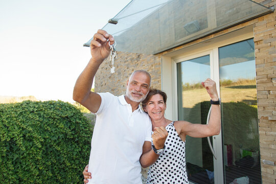 marito e moglie di mezza età mostrano le chiavi di casa mentre sullo sfondo si intravede la loro abitazione