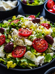 Fresh Greek salad - feta cheese, tomatoes, cucumber, lettuce, black olives and onion on wooden table