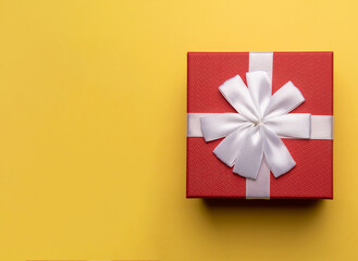 Red gift box with white bow on yellow background,flat lay