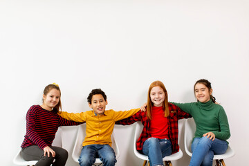 Portrait of cute little kids in jeans  sitting in chairs against white wall