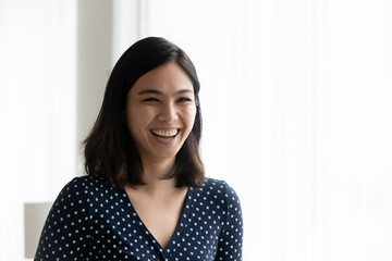 Head shot happy emotional millennial mixed race korean asian woman having fun indoors, laughing at funny joke, enjoying relaxed stress free moment, copy space free place for advertising text.