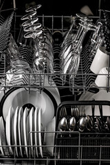 Clean dishes in the dishwasher. Wine glasses, glasses, cups, plates, cutlery. Close-up. Washing-up and housework concept. Vertical shot