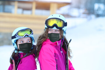 young sisters have fun on the ski slope in helmets and masks on face
