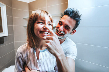 Young couple having fun playing with shaving foam in the bathroom - Boyfriend and girlfriend...