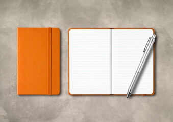 Orange closed and open lined notebooks with a pen on concrete background